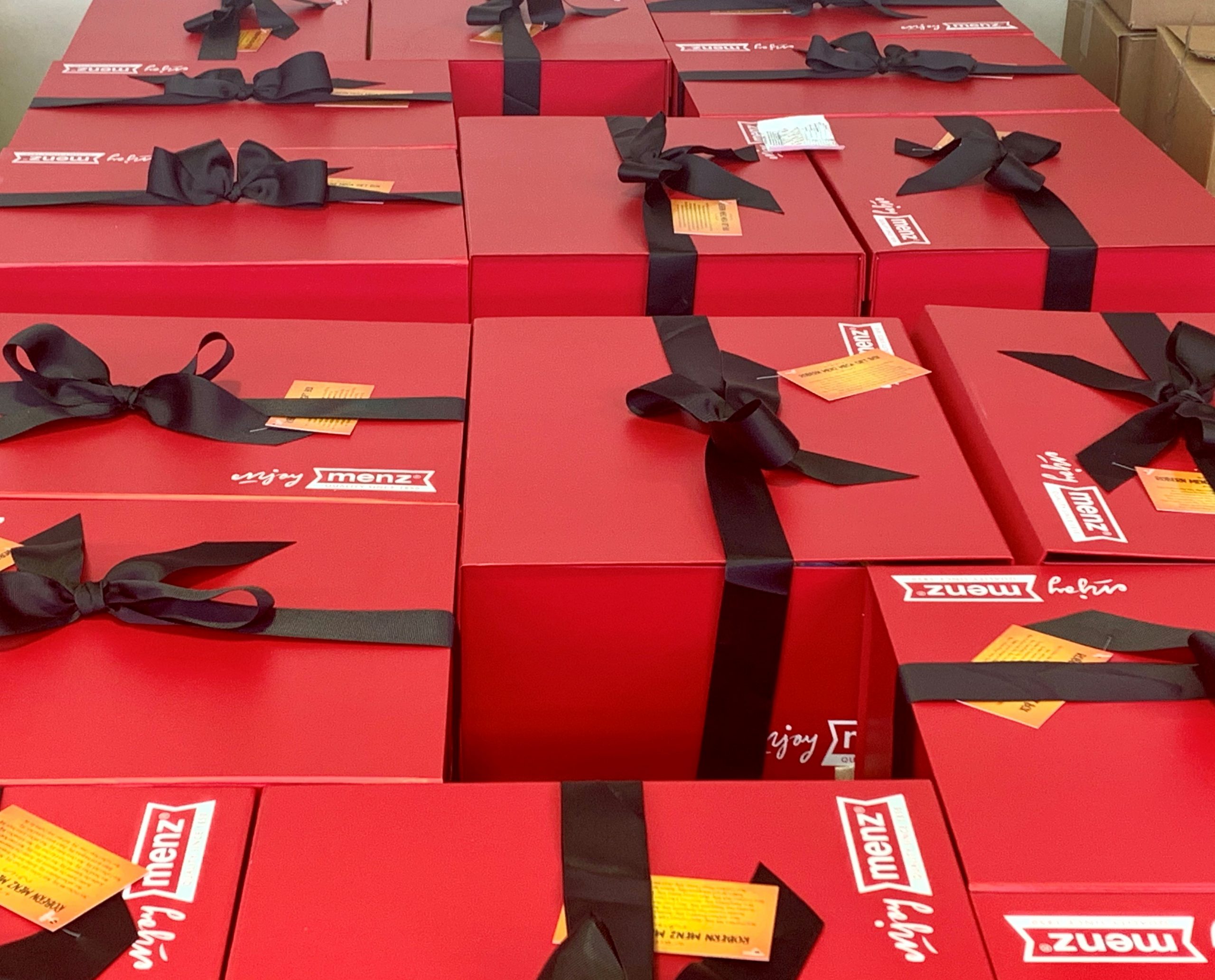 Red packaging boxes stacked next to each other. Black ribbon tied around packages with bow on top.