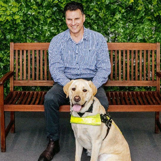 Man sitting on park bench with Guide Dog sitting in front
