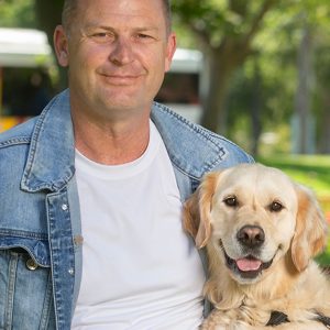 White middle aged man smiling at the camera next to a yellow Dog