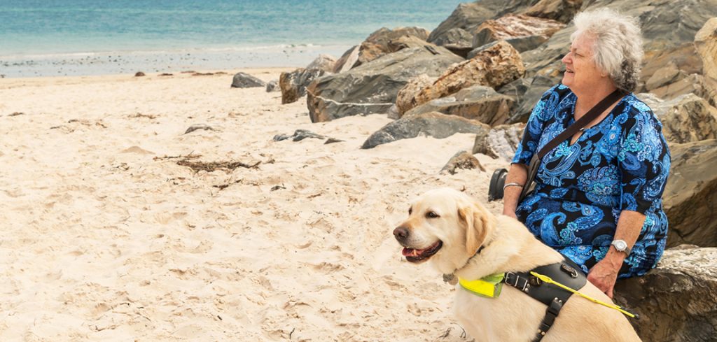 Cheryl and her Guide Dog Winston sitting on the beach